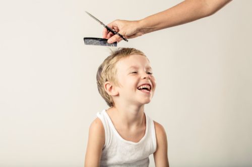 A young boy getting a haircut with his eyes on the scissors.